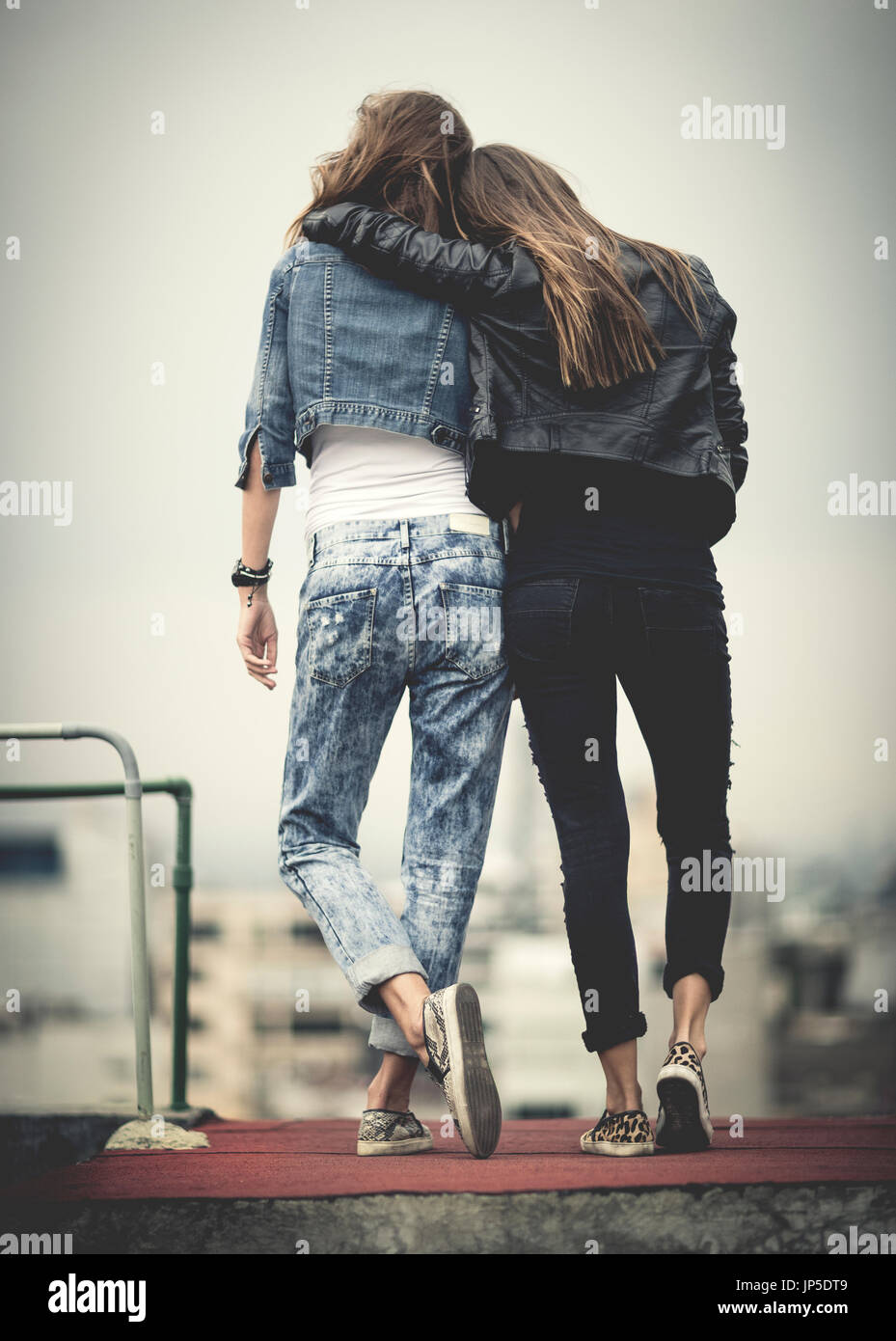 rear view of young woman standing on a rooftop with their arms around ...