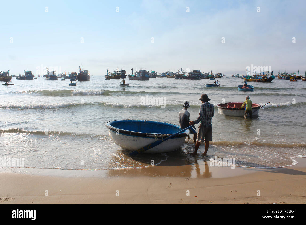 Mui Ne, Vietnam - June 27, 2017: Crowded scene of daily early morning fish market on beach with the fishermen resting on round boat Stock Photo