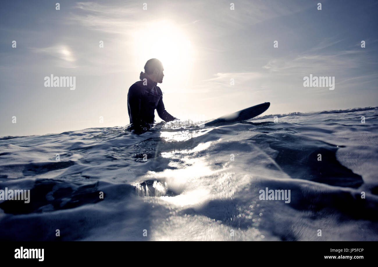 Surfer wearing wetsuit sitting on surfboard in the ocean Stock Photo ...