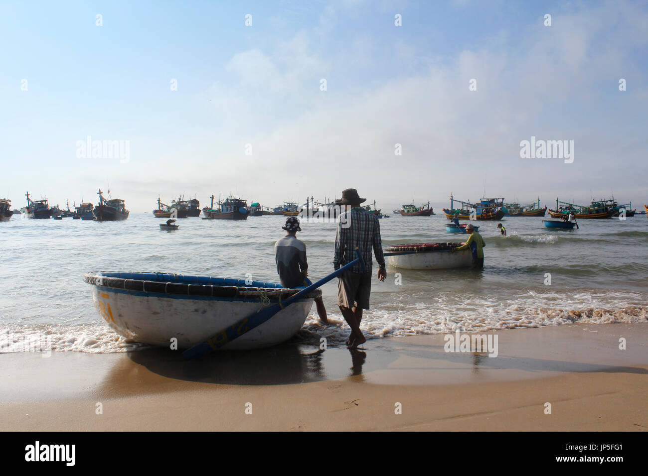 Mui Ne, Vietnam - June 27, 2017: Crowded scene of daily early morning fish market on beach with the fishermen resting on round boat Stock Photo