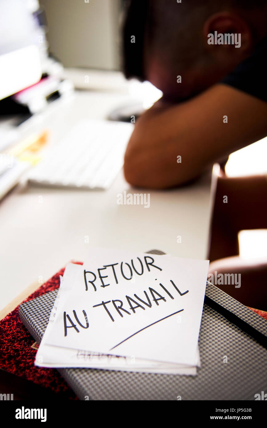 closeup of a concerned man sitting at his office desk and a note in the foreground with the text retour au travail, back to work written in french Stock Photo