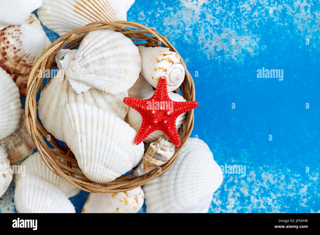 Various seashells in woven basket on blue rustic background. Top view with copy space Stock Photo
