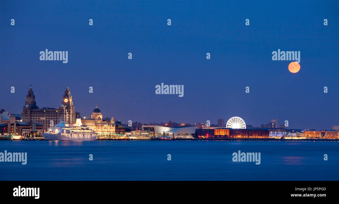 Moon over Liverpool waterfront. An orange moon adds drama to this panorama of the Liverpool skyline at night. Stock Photo