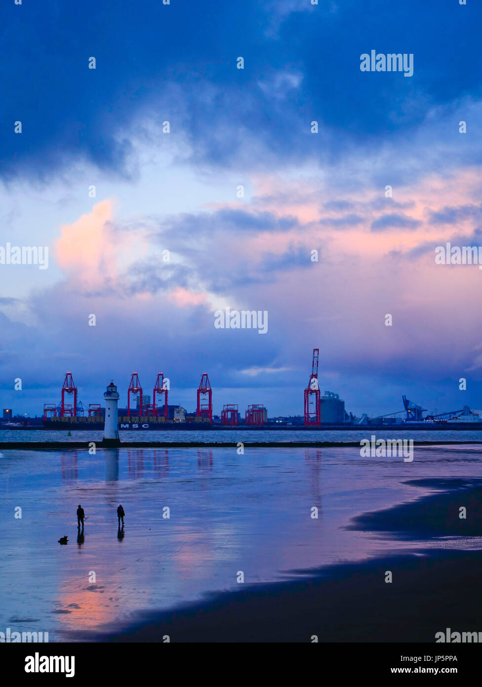 Giant cranes at Liverpool TWO container port shown against the backdrop of a dramatic evening sky with reflections in the River Mersey at low tide. Stock Photo