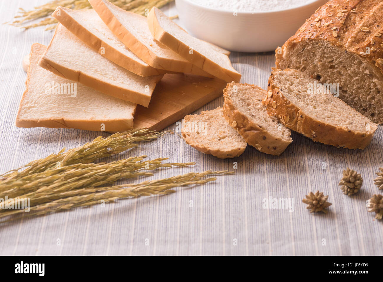 Freshly baked traditional wheat bread and wheat and  oat on white pattern linen tablecloth, soft focus Stock Photo