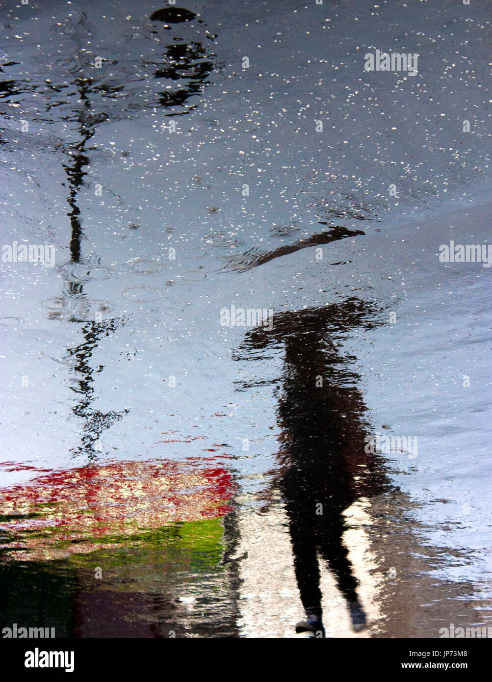Blurry person under umbrella reflection shadow silhouette on rainy city street asphalt sidewalk Stock Photo