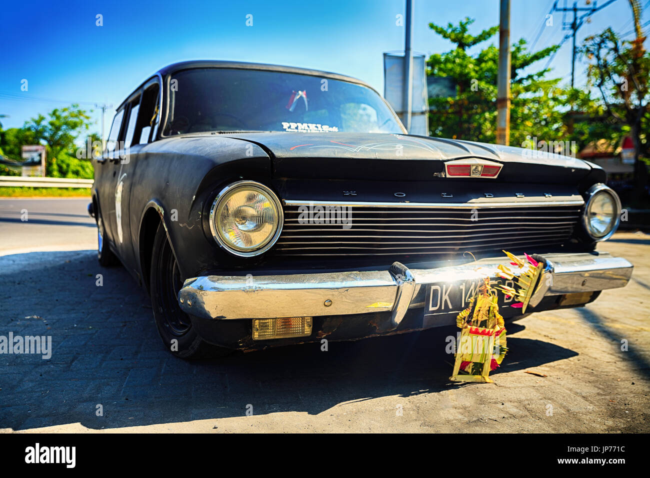 Old and reliable Classic vintage retro Holden car with chrome mirror bumper on background street in ubud on background blue sky / Indonesia Stock Photo