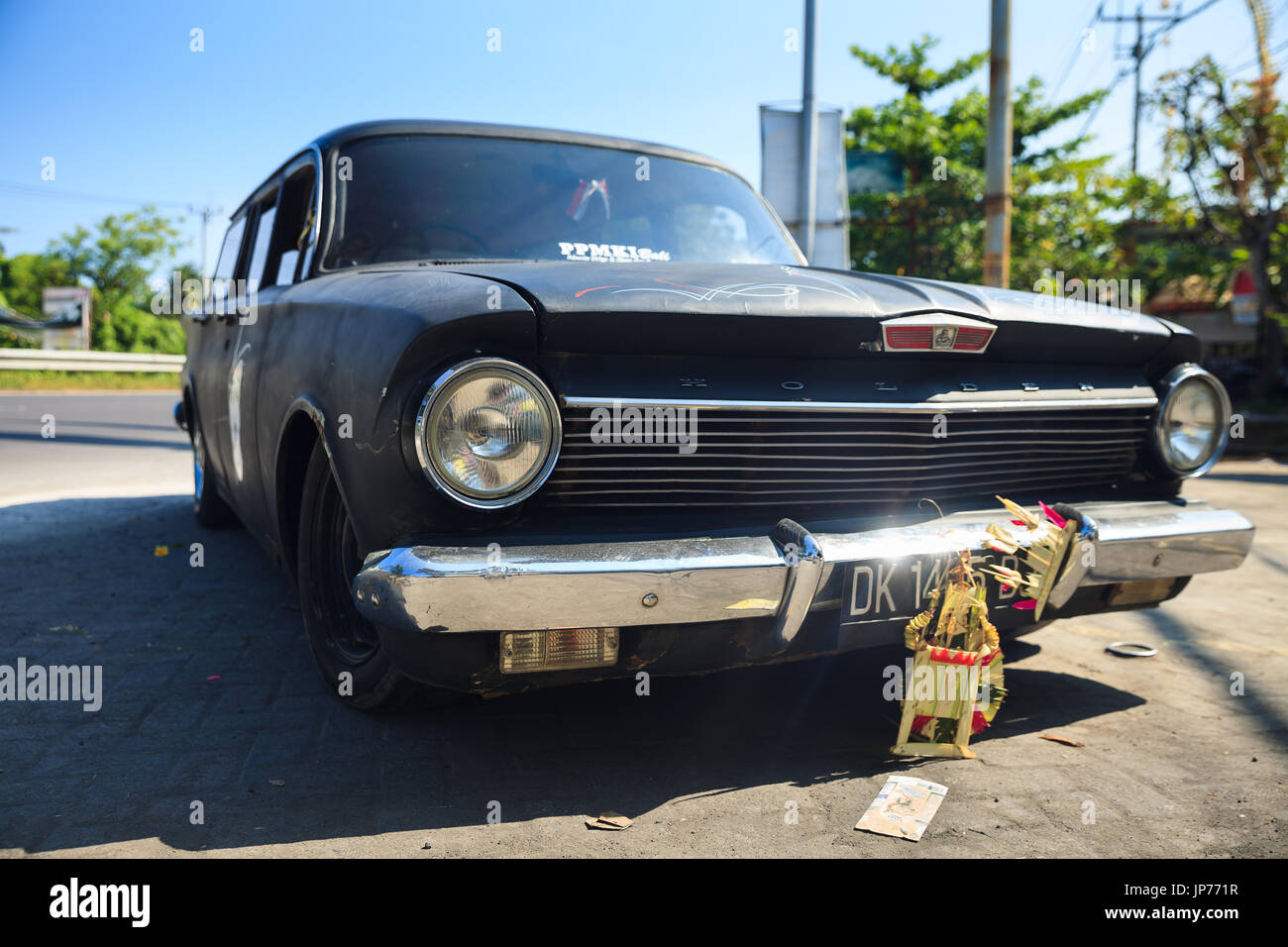 Old and reliable Classic vintage retro Holden car with chrome mirror bumper on background street in ubud on background blue sky / Indonesia Stock Photo