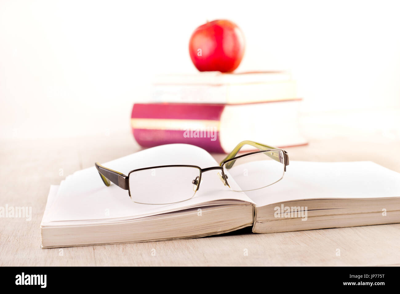 Close up of reading glasses on open book on desk with pile of literatures and apple in background Stock Photo