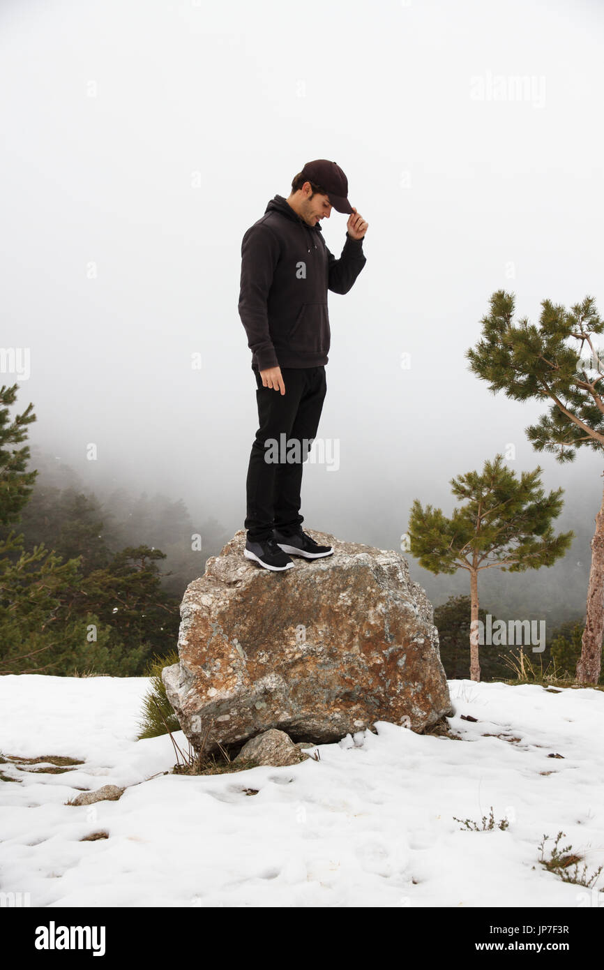 Handsome caucasian young man climbed up a rock in the mountain on a snowy day with foggy background - freedom, joy, goals, positivity, sport concept Stock Photo