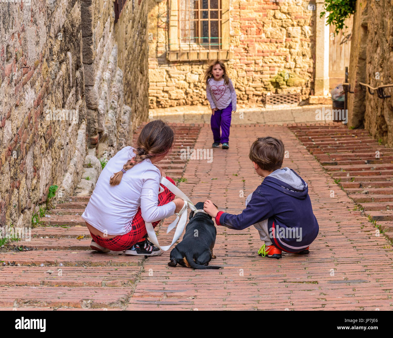 COLLE VAL D'ELSA, ITALY - APRIL 25, 2017 - Two kids play with a puppy dog in an alley of Colle Val d'Elsa. Stock Photo