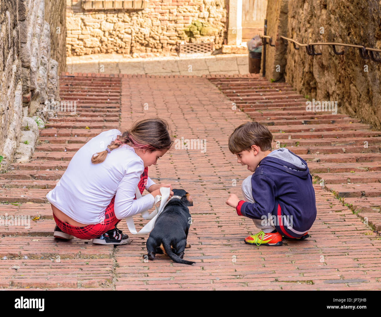 COLLE VAL D'ELSA, ITALY - APRIL 25, 2017 - Two kids play with a puppy dog in an alley of Colle Val d'Elsa. Stock Photo