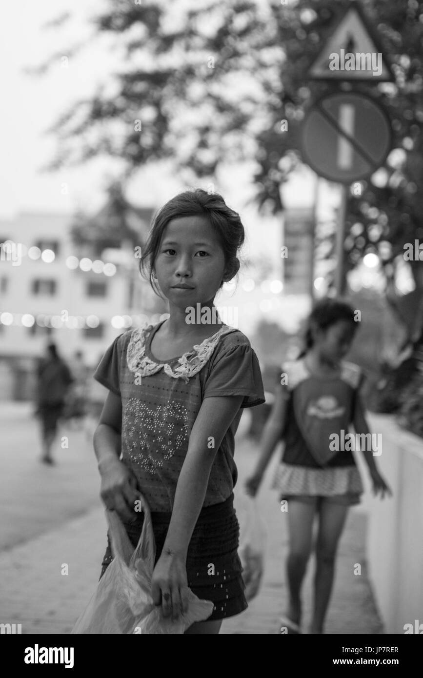 LUANG PRABANG, LAOS - MARCH 12, 2017: Black and white and vertical picture of Lao girl going to Buddhist Alms Giving Ceremony, where local people offe Stock Photo