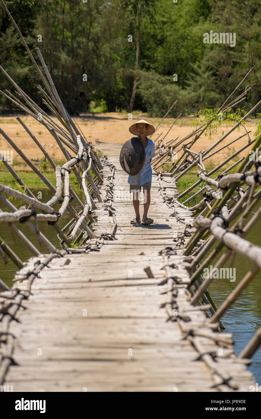 Vietnamese man walking across a traditional bamboo bridge in rural Vietnam Stock Photo