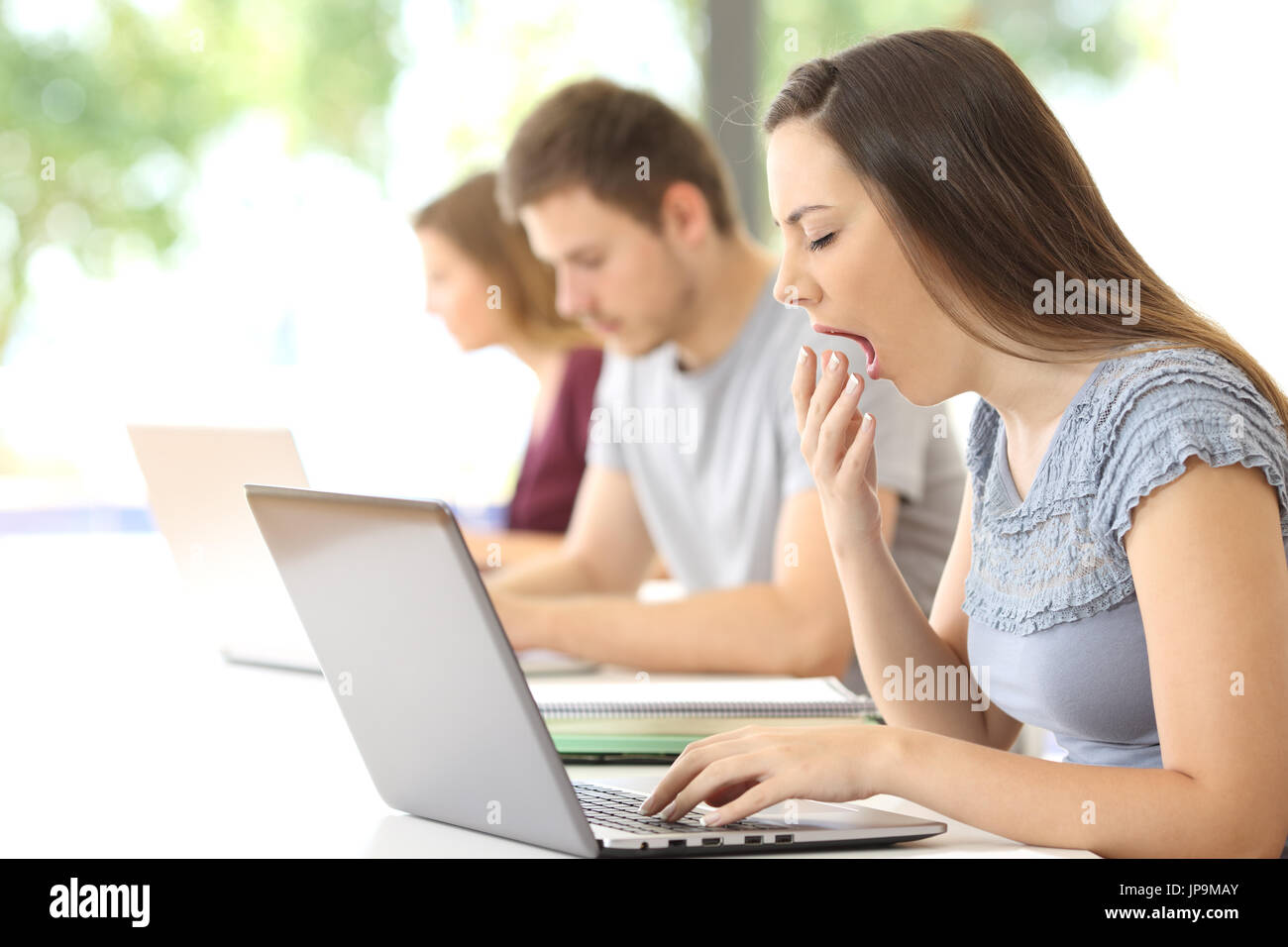 Side view of a tired student yawning using a laptop at classroom Stock Photo