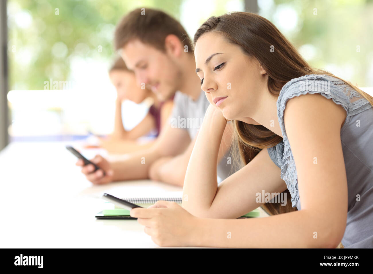 Side view of three bad students distracted using smart phones during a class in a classroom Stock Photo