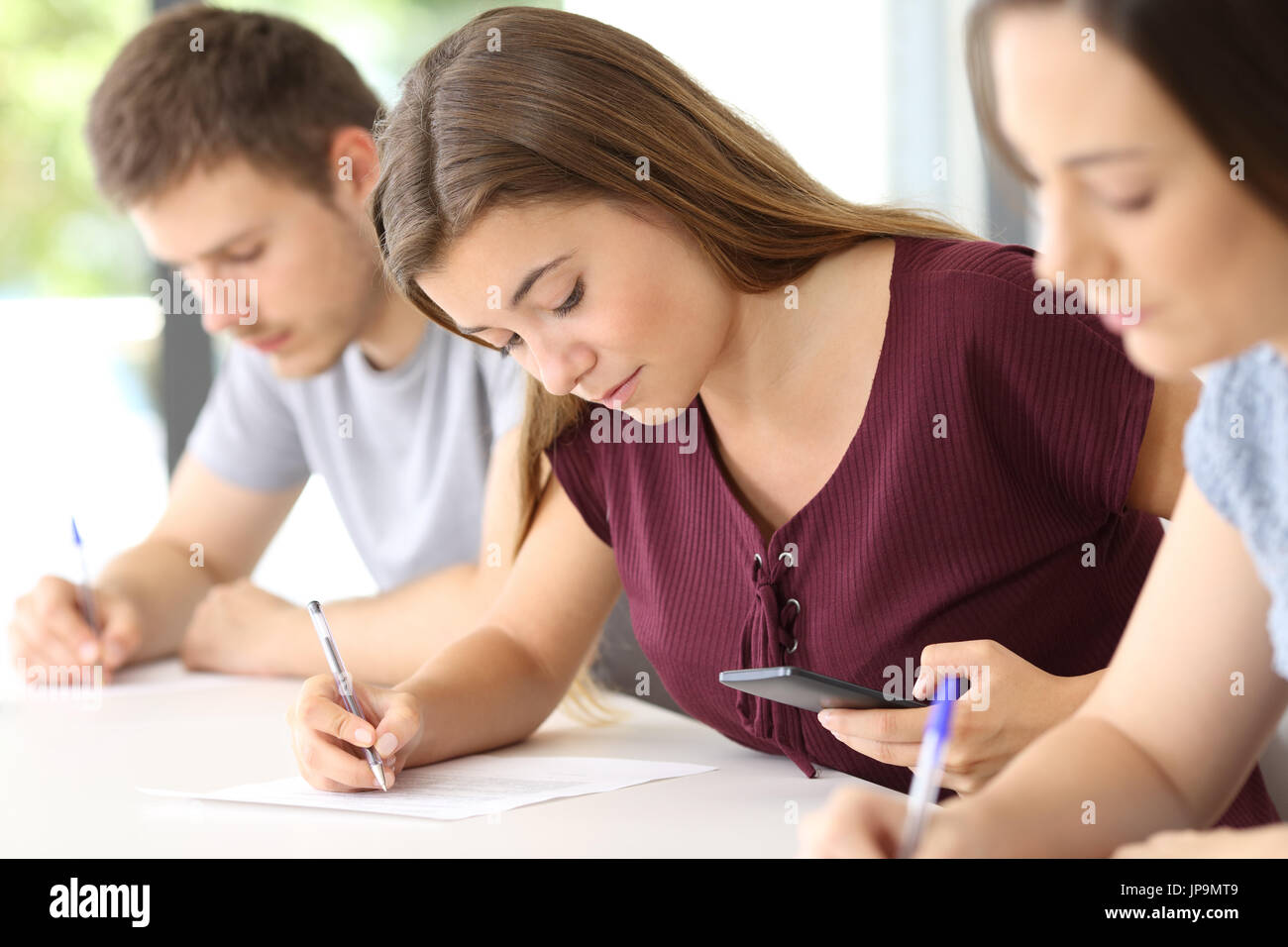 Student using a smart phone to copy during an exam in a classroom Stock Photo