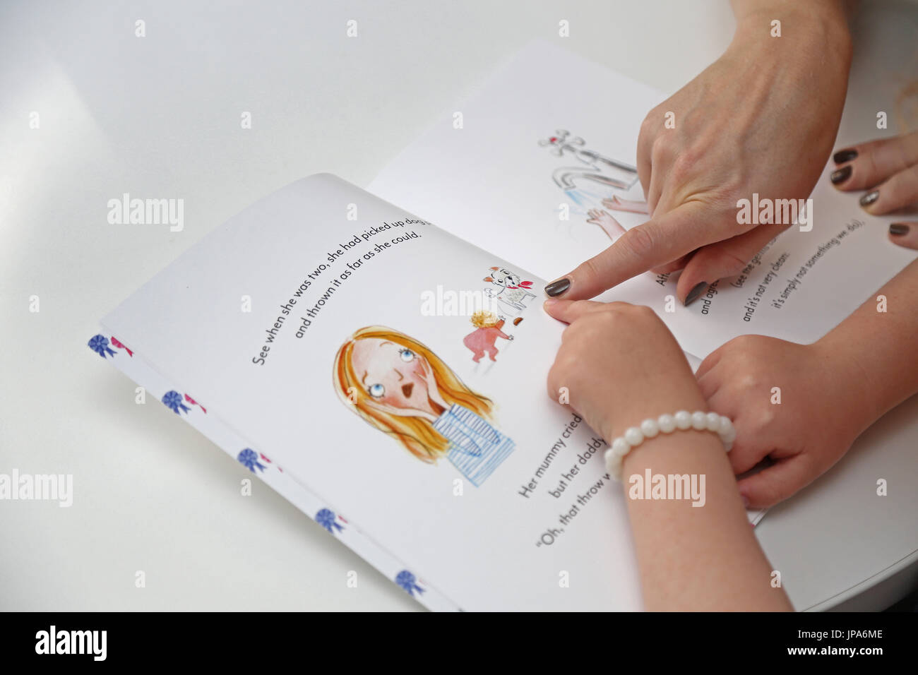 A mother and daughter point and read from a book by new children's author Suzanne Hemming. Shows only the book and forearms. Stock Photo