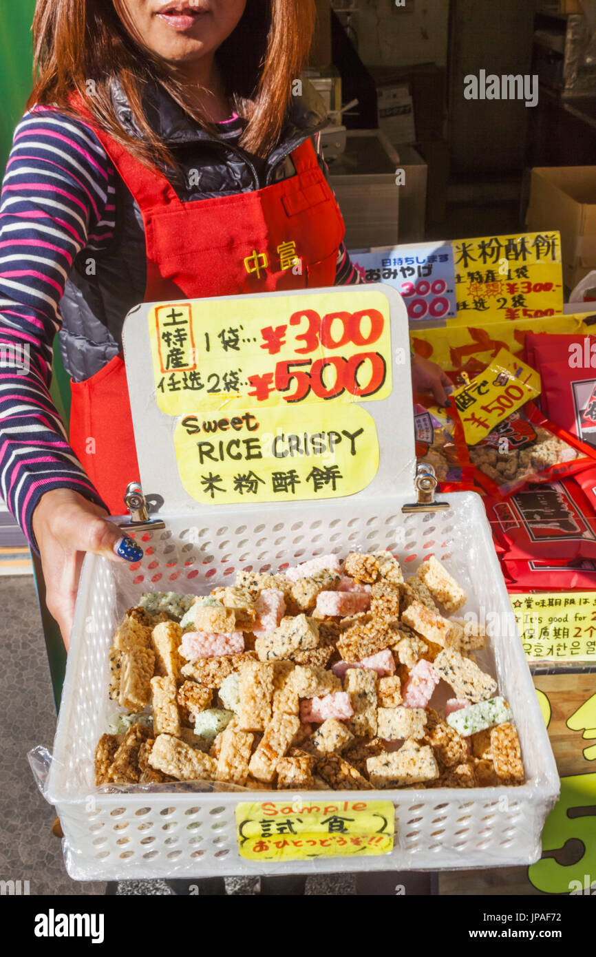 Japan, Honshu, Tokyo, Asakusa, Sensoji Temple aka Asakusa Kannon Temple, Nakamise Shopping Street, Girl Offering Free Samples of Traditional Sweets Stock Photo