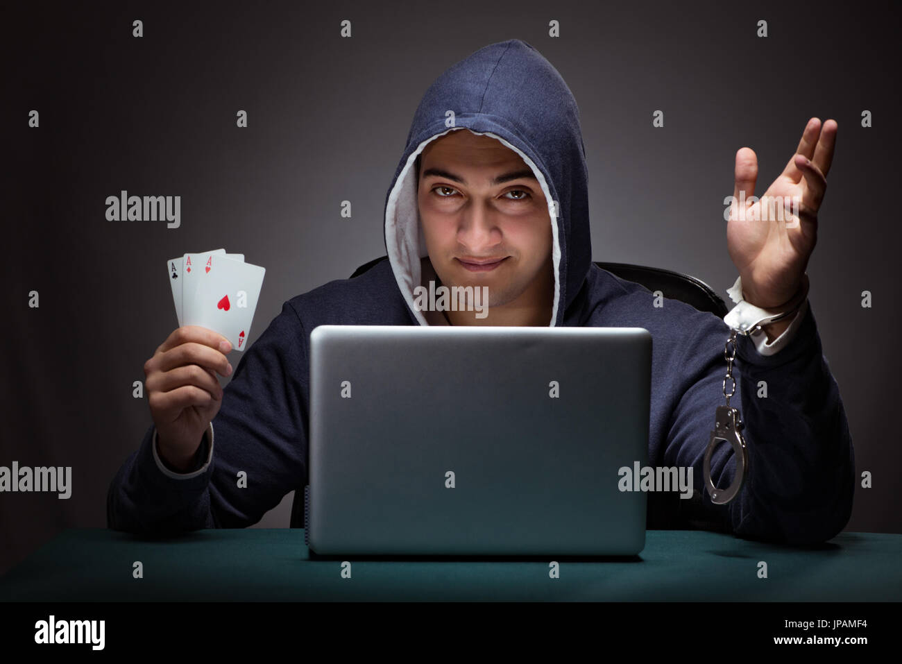 Young man in handcuffs wearing a hoodie sitting in front of a laptop computer gambling Stock Photo