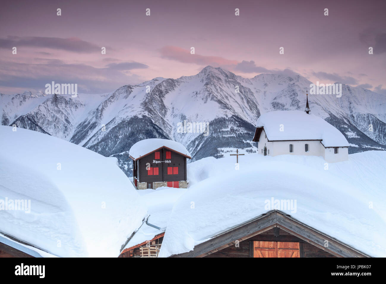 Pink sky at sunset frames the snowy mountain huts and church Bettmeralp district of Raron canton of Valais Switzerland Europe Stock Photo
