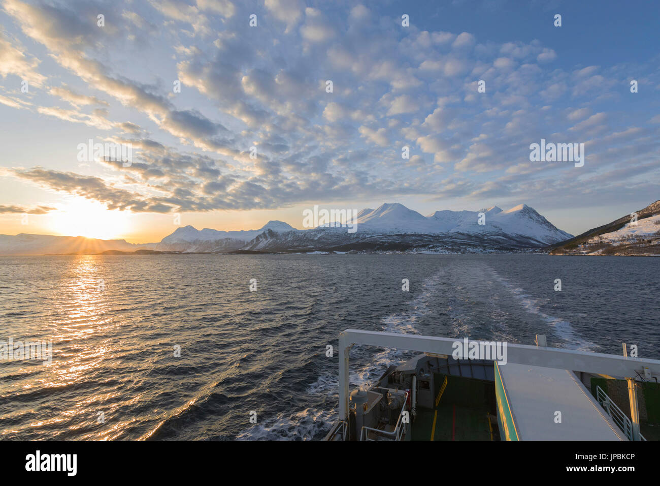 Ferry in the cold sea proceeds on its way to Lyngseidet lighted up by sunset Lyngen Fjord Lyngen Alps Tromsø Norway Europe Stock Photo