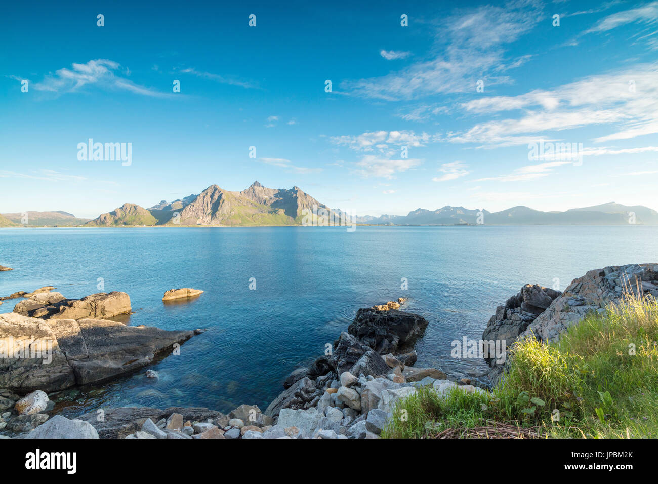 Sun shines on the blue sea and the rocky peaks at night during summer Vikten Nord Trøndelag Lofoten Islands Norway Europe Stock Photo