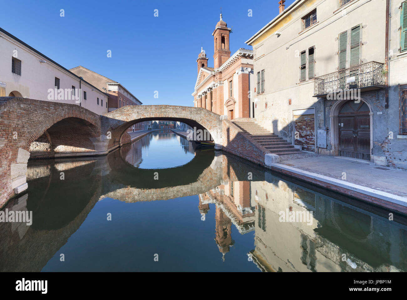 Europe, Italy, Emilia Romagna, Ferrara, Comacchio. Typical Small bricks bridges over the water canal and the St Peter church Stock Photo