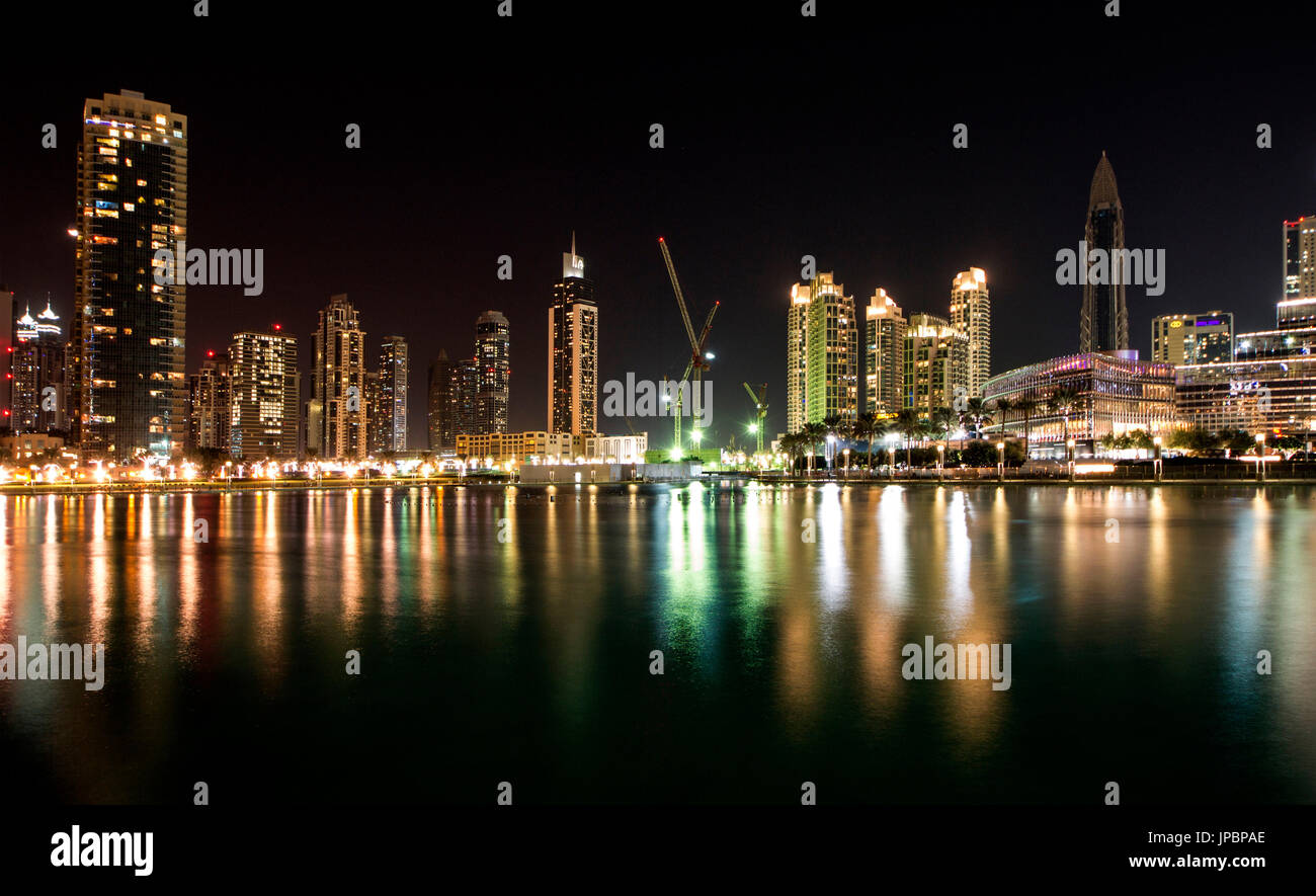 The night skyline show the sequence of bright skyscrapers which are reflected on the water of Burj Khalifa lake. Dubai, United Arab Emirates Stock Photo