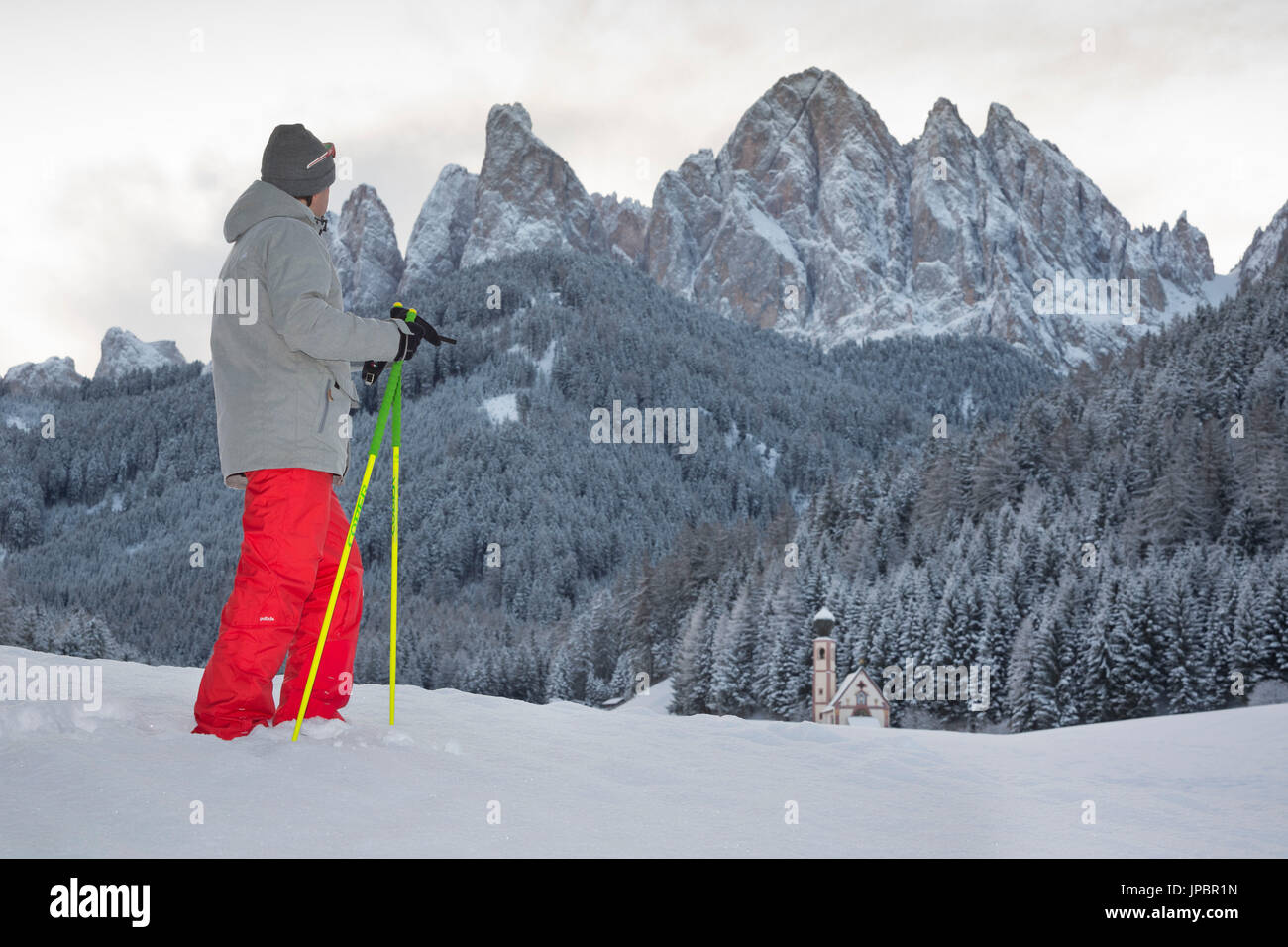 a view of a winter trekking in Villnöss with one person looking to the church of S. John in Ranui and the Geisler in the background, Bolzano province, South Tyrol, Trentino Alto Adige, Italy, Europe Stock Photo