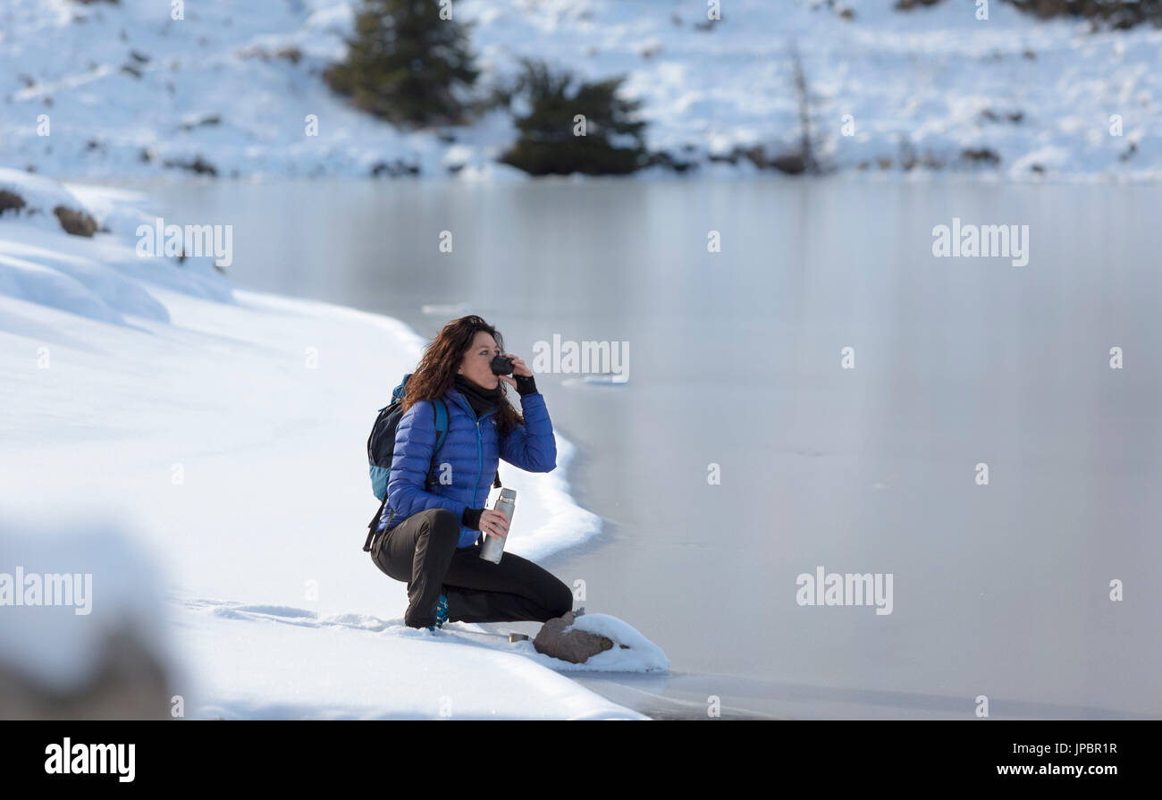 a view of a winter trekking where the woman sits by the lake and drink a cup of tea, Colbricon Lake, Trento province, Trentino Alto Adige, Italy, Europe Stock Photo