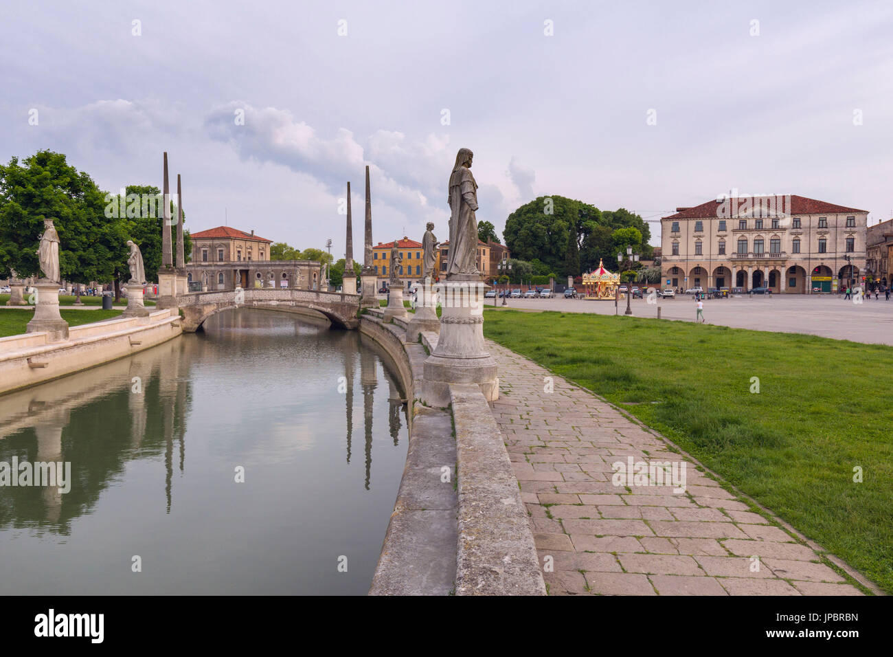 View of the Prato della Valle, Padua, Italy on an overcast day with reflections of the statues in the water of the elliptical canal and an historic building in the background, veneto, italy, europe Stock Photo