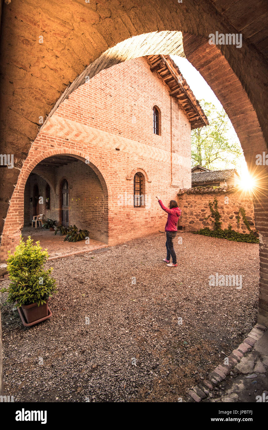 Grazzano Visconti, Vigolzone, Piacenza district, Emilia Romagna, Italy. Woman standing on a couryard of brick houses. Stock Photo
