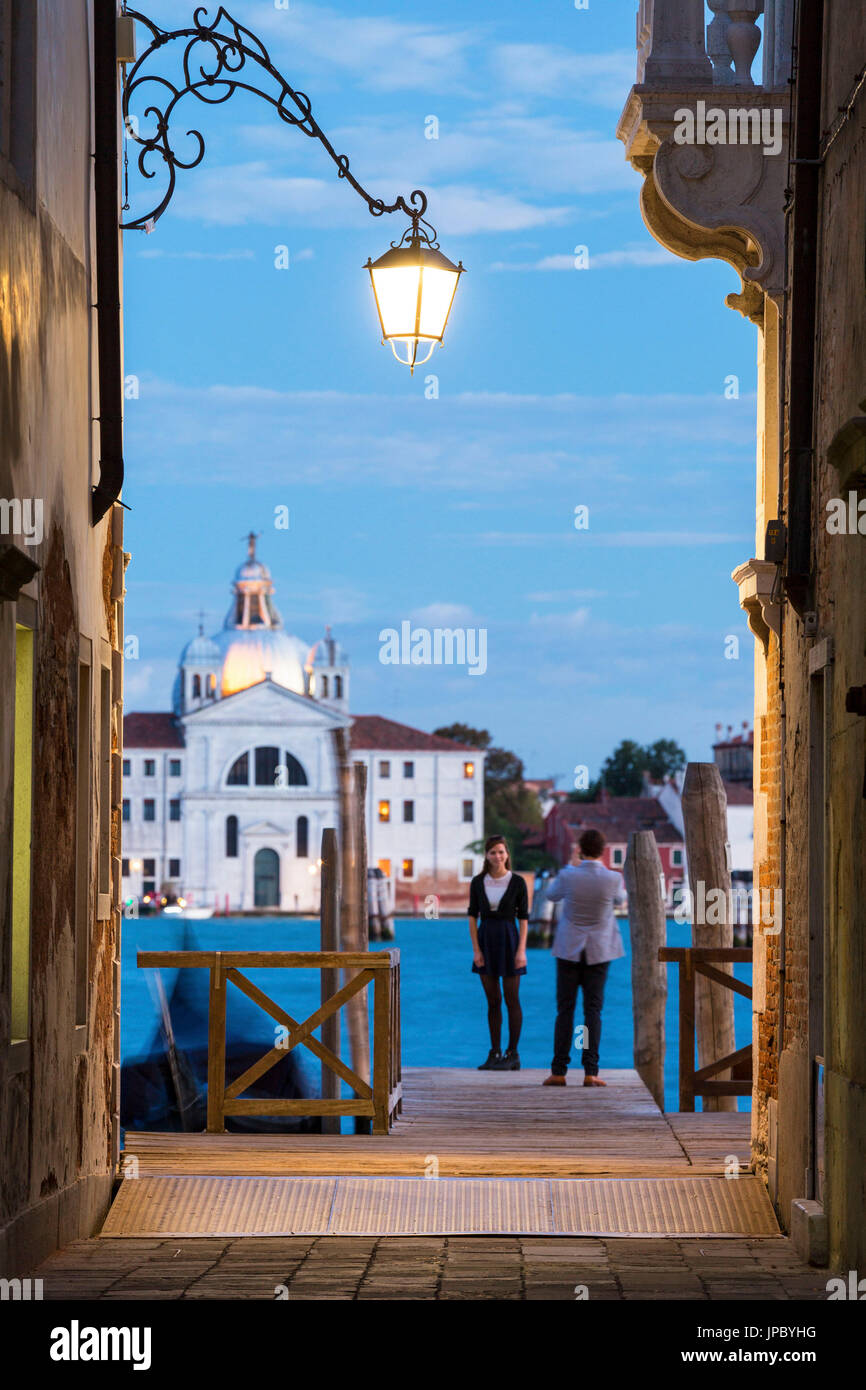 Tourists on the wood pier with the church Le Zitelle in the background framed by the lights of dusk Venice Veneto Italy Europe Stock Photo