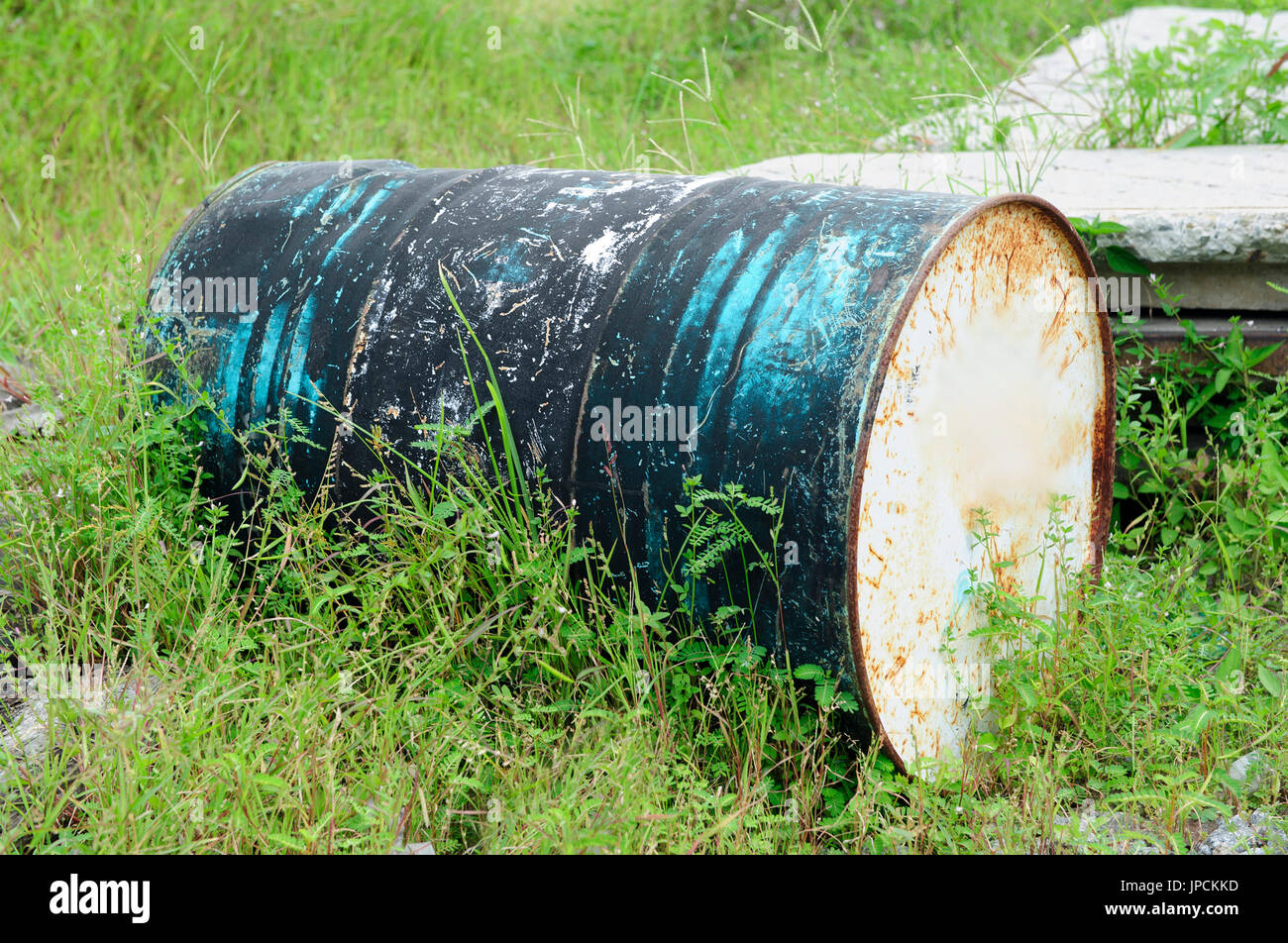 Papar , Sabah , Malaysia : an abandoned rusted steel black and blue color barrel half covered by bushy grasses in a grass field Stock Photo