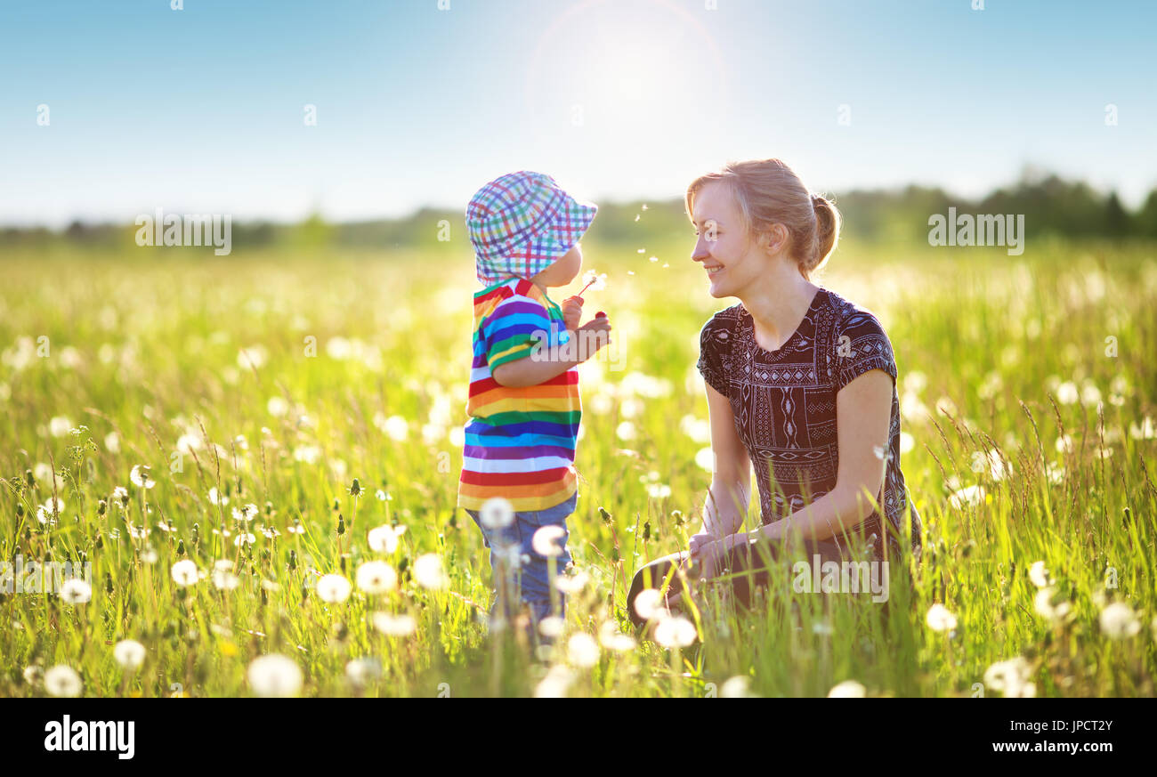 Young woman with a boy blowing dandelions. Mother and son having fun on ...