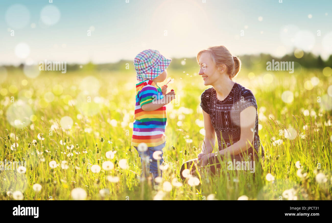 Young woman with a boy blowing dandelions. Mother and son having fun on ...