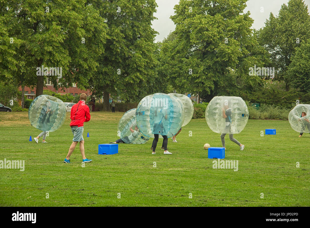 Young men and women play in Bubble Bump new and fun team game outdoor. Peopel are inside of blown plastic transparent bubble shock each other with fun Stock Photo