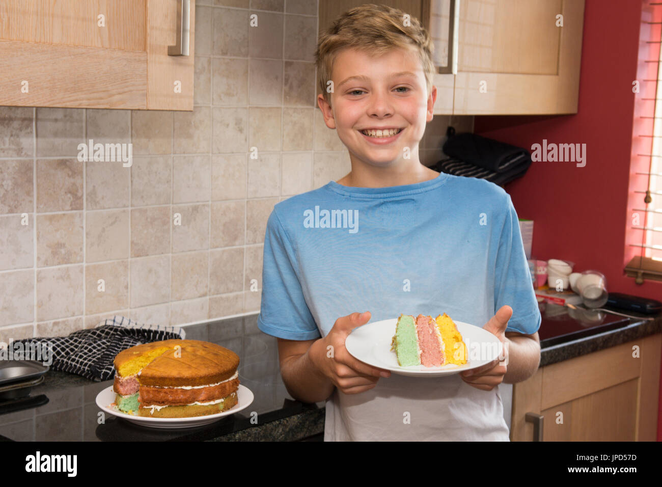 ten year old boy in kitchen showing a rainbow cake he is proud of