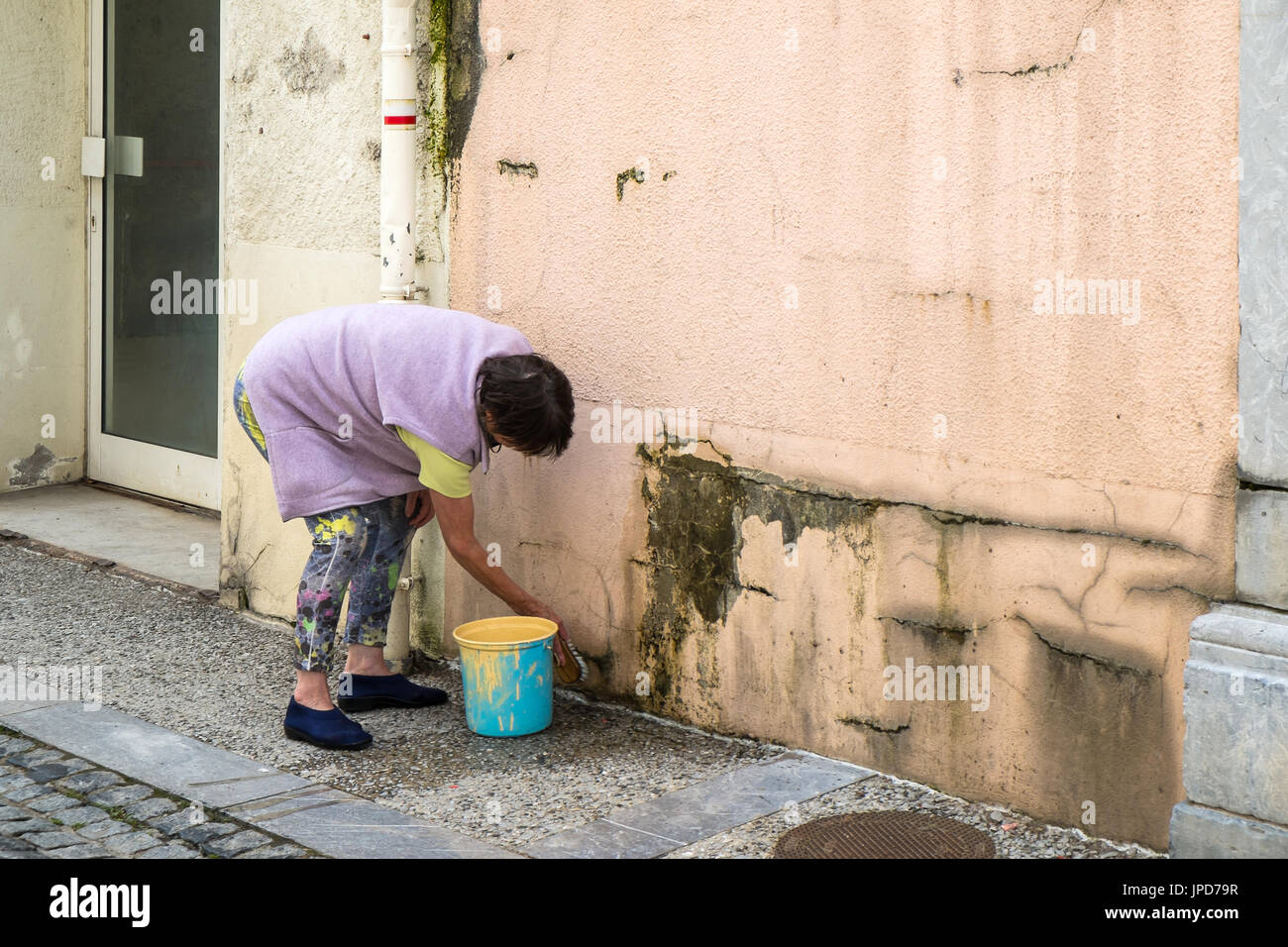 Woman washing dirth outside wall, Laruns, France. Stock Photo