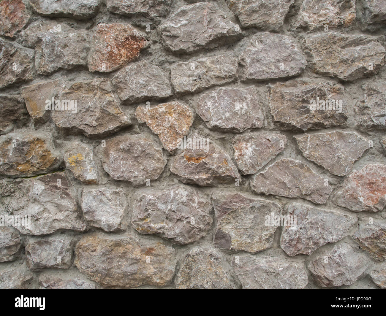 Background. The wall of multi-coloured stones agglomerated with cement mortar Stock Photo
