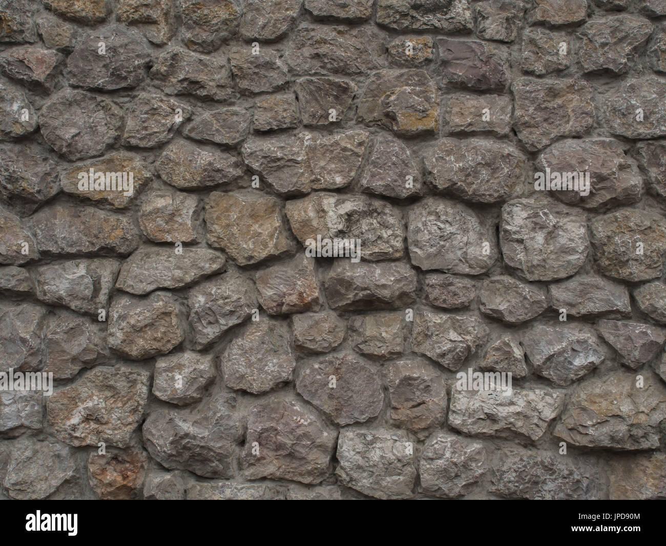 Background. The wall of multi-coloured stones agglomerated with cement mortar Stock Photo