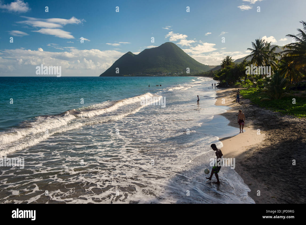 Le Diamant Beach in Martinique, with young man playing with a ball and Sleeping Woman mountain in background Stock Photo
