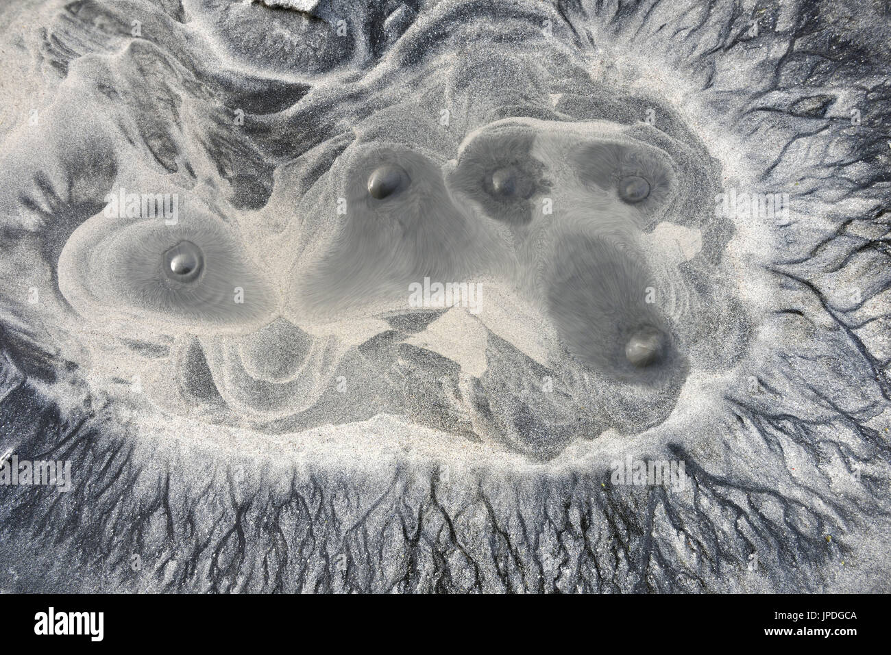 Water oozing out on the surface of a sandy beach forming bizarre shapes ...