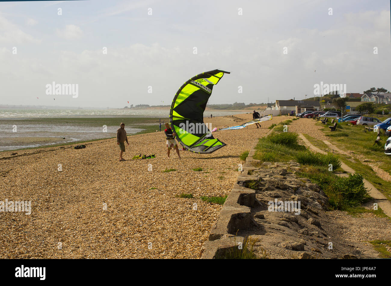 A couple of young men struggle against a stiff breeze to prepare their para glider for an afternoons sport at the beach in Titchfield, Hampshire in th Stock Photo