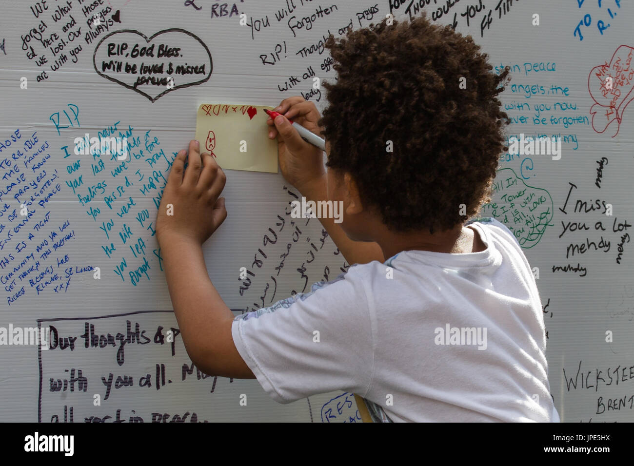 A young boy draws a message on the memorial wall for those who lost their lives in the Grenfell Tower fire. Stock Photo