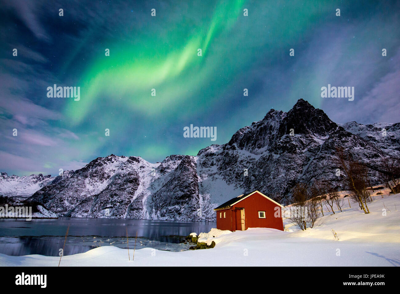 Lofoten, Svoelver, Aurora Borealis over a frozen lake and red rorbu, Norway. Stock Photo