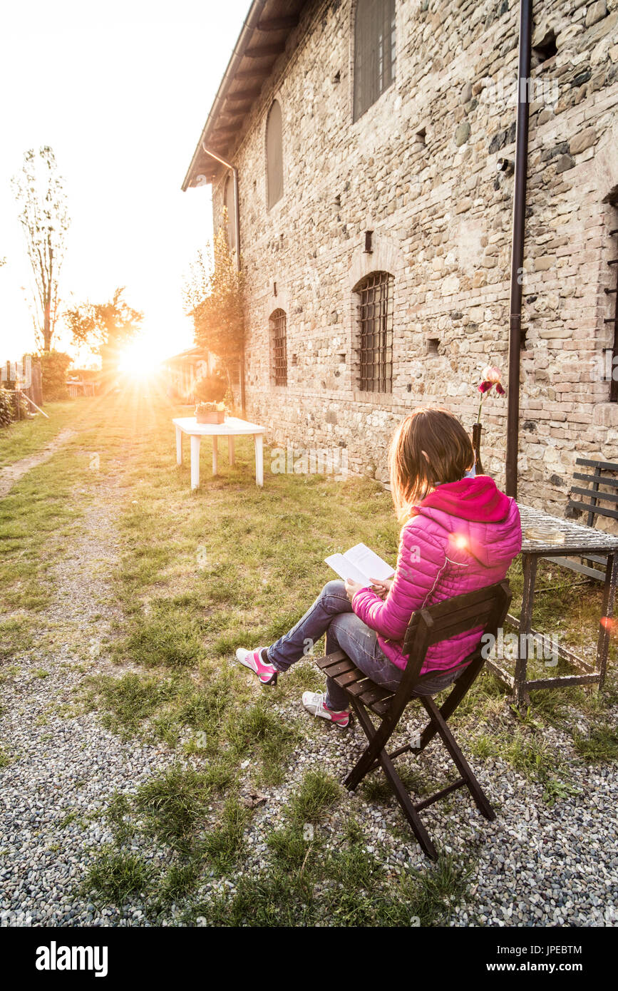 Grazzano Visconti, Vigolzone, Piacenza district, Emilia Romagna, Italy. Woman reading on a chair in a old couryard of the town. Stock Photo
