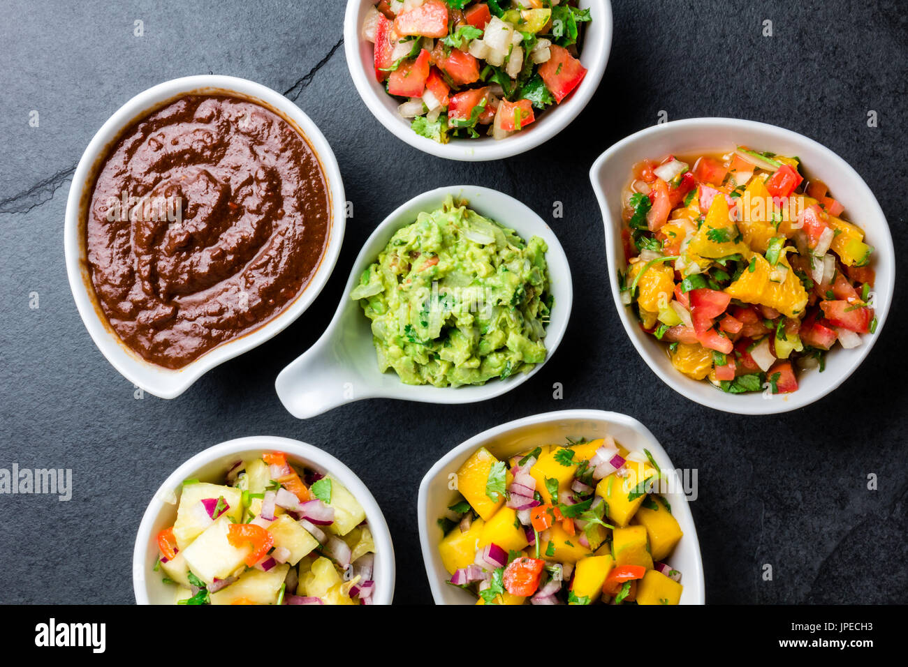 Traditional famous mexican sauces chocolate chili mole poblano, pico de gallo, avocado guacamole, salsa bandera, pinapple salsa, mango salsa on slate Stock Photo