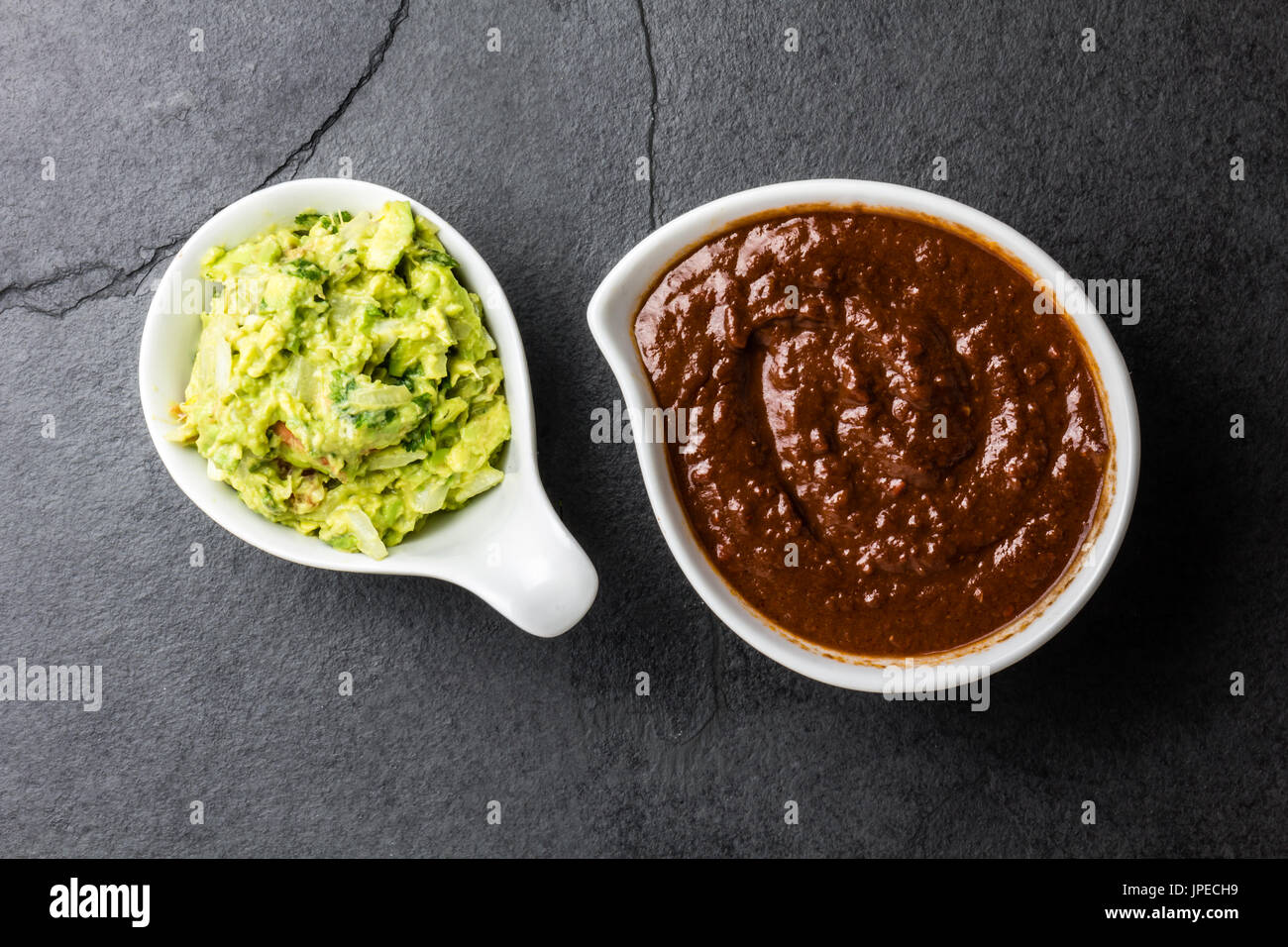 Traditional famous mexican sauces chocolate chili mole poblano, and avocado guacamole on slate gray background. Stock Photo